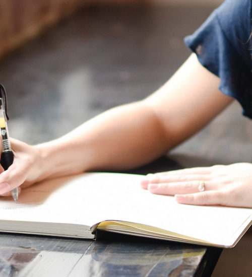 Kvinna sitter vid fönsterbord och skriver för hand.