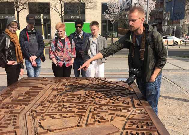 Studerande på rundvandring i Berlin. De står och tittar på ett monument som är en karta över staden.