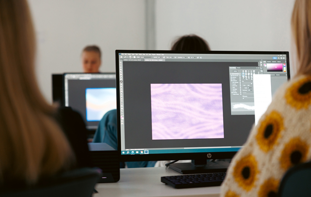 På bilden ser man några datorskärmar och ryggen av studerande som sitter vid datorerna. På skärmen ser man att de jobbar med något grafiskt program.