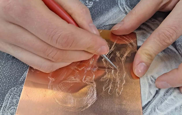 Lähikuva käsistä, jotka piirtävät kuivaneulatekniikalla kuparilevylle grafiikka tunnilla.